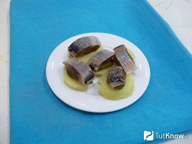 На ломтики картофеля выложен кружочек помидор, а сверху кусочек селедки