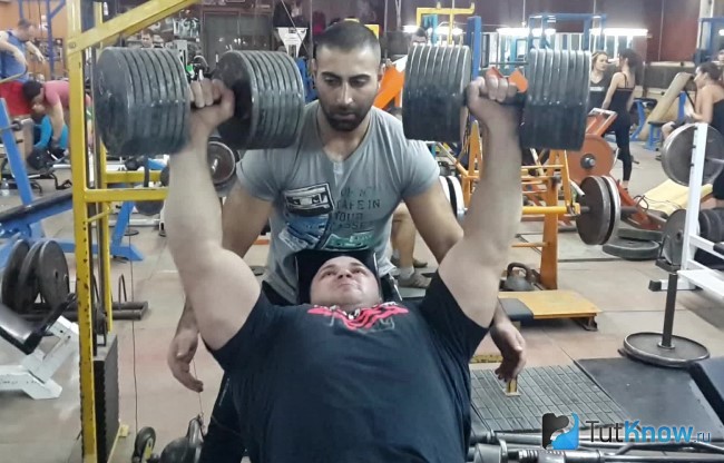 Атлет выполняет жим гантелей лёжа