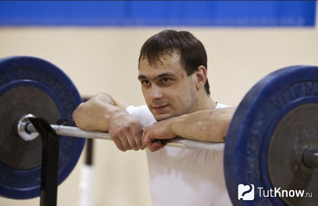 Спорстмен в зале стоит возле штанги