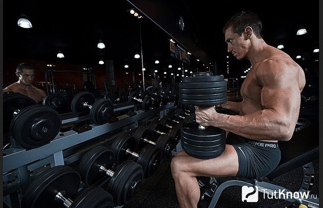 Спортсмен сидит с гантелями перед зеркалом