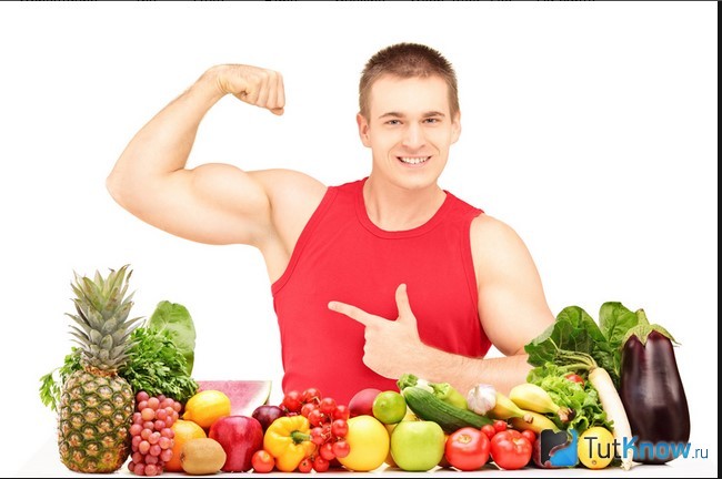 Атлет демонстрирует мышцы возле фруктов и овощей