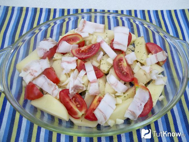 Картофель, помидоры, чеснок и сало выложены в форму для запекания