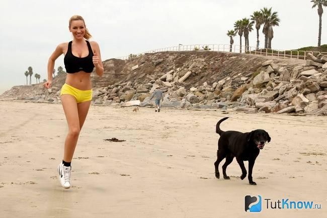 Девушка бежит со своей собакой по пляжу