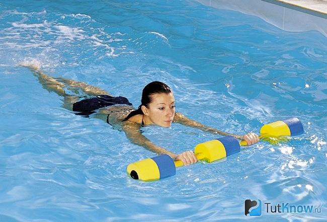 Девушка тренируется в бассейне со специальными гантелями