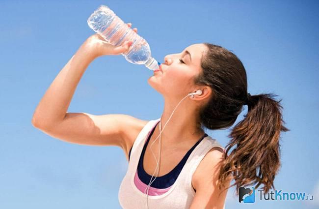 Девушка в наушниках пьёт воду