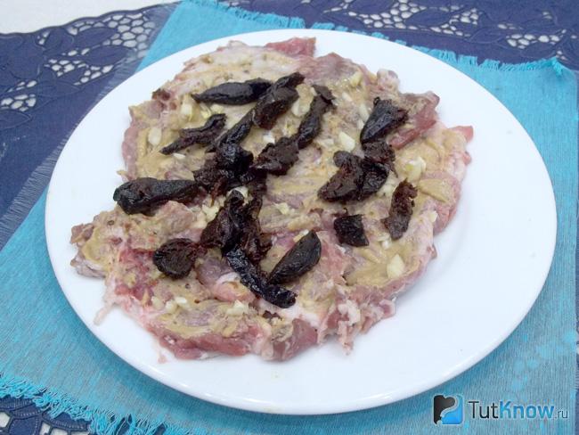 На мясо выложен нарезанный чеснок и чернослив