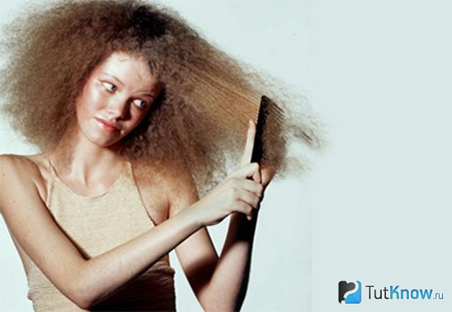 Девушка пытается расчесать свои пушащиеся волосы