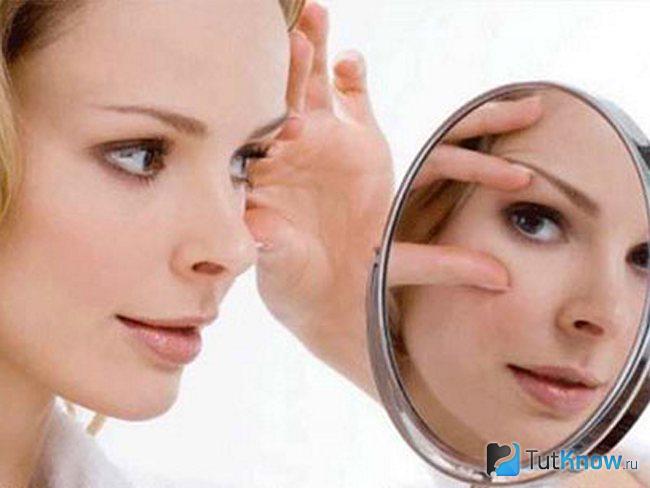 Женщина осматривает в зеркале область вокруг своих глаз