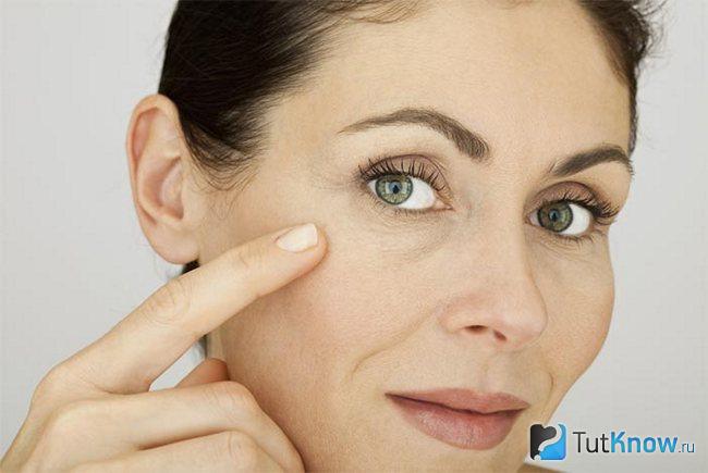 Женщина в возрасте за 40 лет проводит пальцем по коже возле глаза