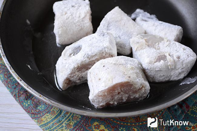 Кусочки хека в муке лежат на сковороде