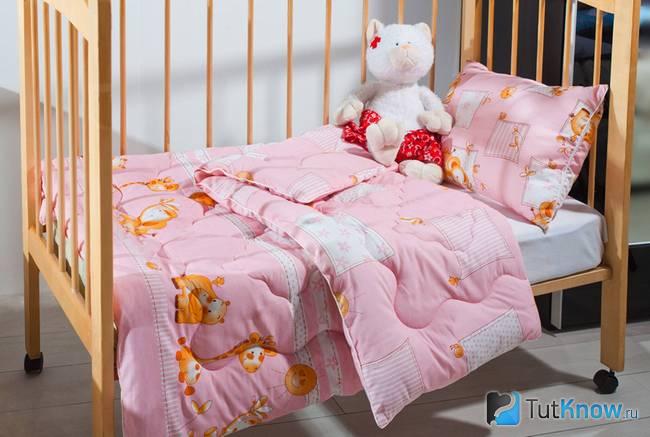 Розовая подушка и одеяло застелены на кроватке