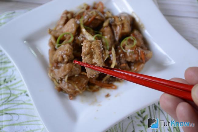 Кусочек свинины удерживается китайской палочкой
