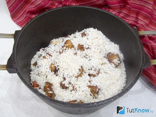 В казан к продуктам для рассыпчатого плова с мясом на плите добавлен рис