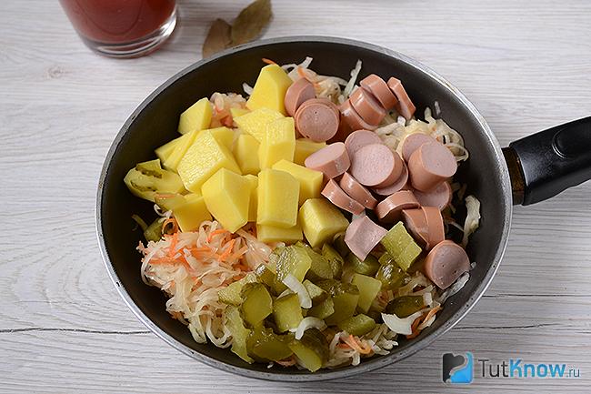 Картошка, солёные огурцы и сосиски выложены на сковородку