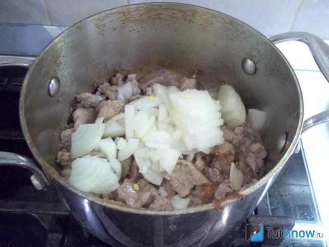 В кастрюлю к обжаренному мясу добавлен нашинкованный лук