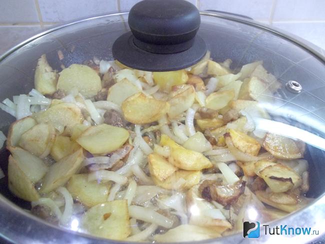 Картофель с луком жарятся в сковороде под крышкой