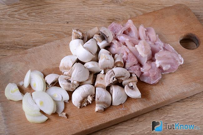 Лук, грибы и куриные бёдрышки нарезаны на кухонной доске