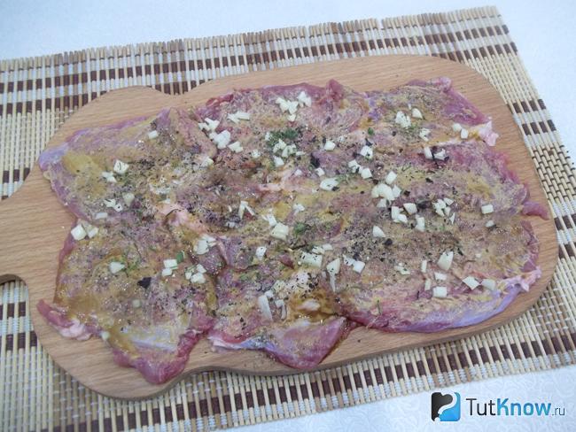 Пласт мяса присыпан рубленым чесноком и зеленью