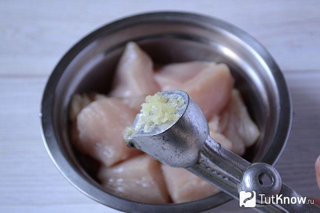 Измельченный чеснок на фоне миски с куриным филе