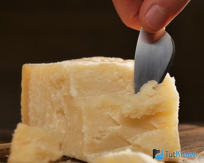 Мужчина отрезает ломтик сыра Грана Падано