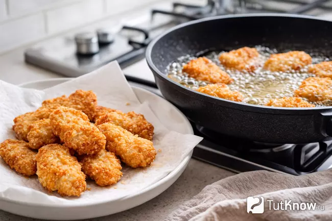 Готовые и жарящиеся куриные наггетсы в панировке на сковороде