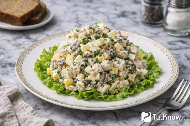 Салат с курицей, яйцами и грибами порционно на тарелке