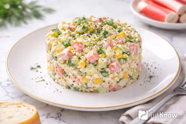 Салат с крабовыми палочками, яйцом и кукурузой подан на тарелке в кулинарном кольце