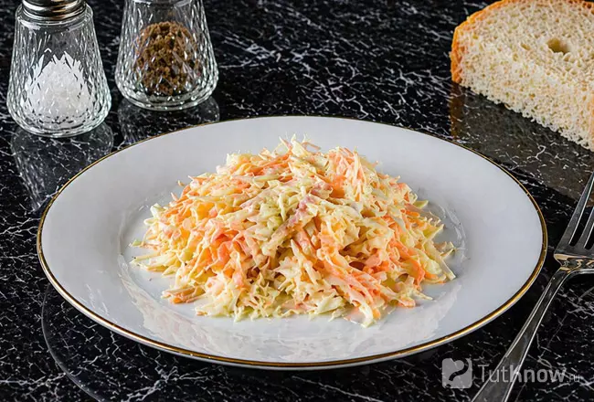 Салат из капусты, яблока и моркови заправленный сметаной на белой тарелке