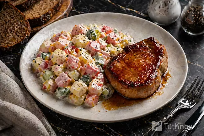 Подача готового салата с кукурузой, ветчиной и помидорами и свиным стейком